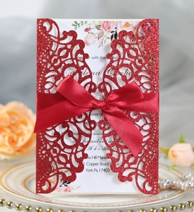 Laser cut red wedding invitation card with ribbon bow on a decorative white plate