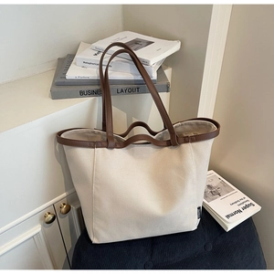 Detail of canvas tote with brown leather trim and brand label in minimalist setting
