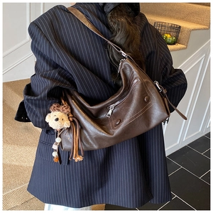 Detail of a dark brown hobo bag with a plush bear charm on a navy striped blazer