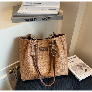 Détail d'un sac cabas tressé marron avec écusson en cuir et bandoulière en chaîne dorée
