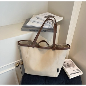 Close-up of cream canvas tote bag with brown leather handles and brand woven label
