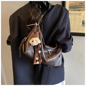 Detail of dark brown leather crossbody bag with silver zipper and plush dog pendant