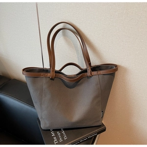Detail view of grey canvas tote bag with brown leather straps and branded side label