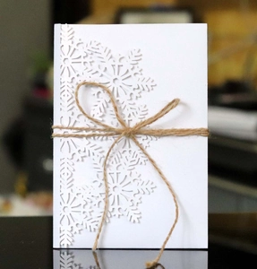 Detail of laser-cut snowflake wedding invitation with rustic brown twine bow knot