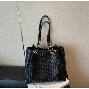 Détail du sac cabas tressé noir avec maillons de chaîne dorés et plaque de marque en métal