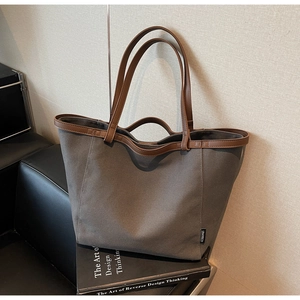 Detailed view of taupe canvas tote bag with brown leather handles on a black book