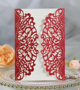 Detail of red glitter laser cut wedding invitation with decorative bow and rose setup
