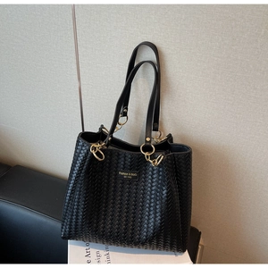 Détail d'un sac cabas tissé noir avec anneaux dorés et lanières en cuir sur magazines