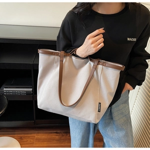 Detail of grey canvas tote bag with brown leather handles and side brand logo