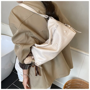 Detailed side view of cream hobo bag with tassel charms and polished faux leather texture