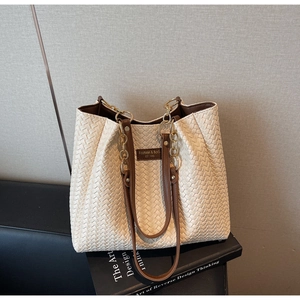 Détail d'un sac cabas tissé beige avec des lanières en cuir marron et des maillons dorés