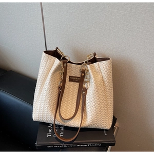 Détail du sac cabas tressé crème montrant les poignées en cuir et la chaîne dorée