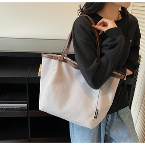 Model wearing large canvas tote bag with brown leather trim and shoulder strap detail