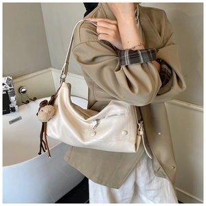 Detail of soft cream leather crossbody bag with decorative zipper and plush bear charm