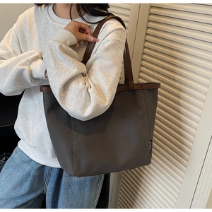 Detail view of large canvas tote bag with dark brown leather trim and side brand tag