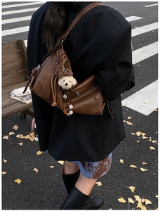 Brown leather shoulder bag with cute plush bear charm and beaded detail in street style
