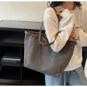 Detail view of large dark grey canvas tote bag with brown leather handles worn on shoulder