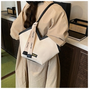 Detail of beige woven tote bag with black leather trim worn by model in trench coat