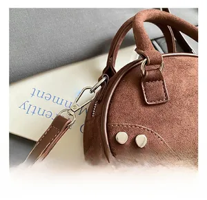Détail de mousqueton argenté et rivets sur un sac bandoulière en daim marron