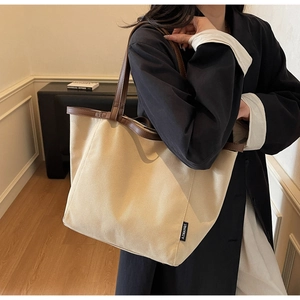 Detail of beige canvas tote bag with brown leather straps and branded woven side label
