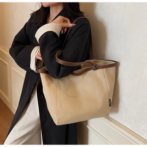 Detail of canvas tote bag with brown leather trim held by a model in a dark blazer