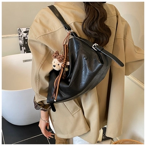 Detail of black matte leather shoulder bag with triangular fold design and bear charm