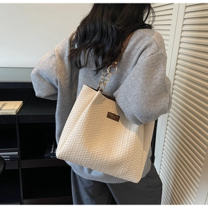 Détail du sac cabas tissé avec tissu crème, poignées en cuir marron et détails de chaîne dorée