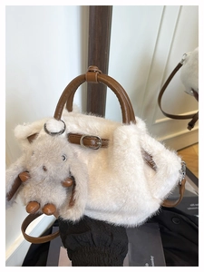 Details einer weißen Kunstpelztasche mit braunen Ledergriffen und Hasenanhänger