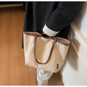 Detail view of beige canvas tote bag with dark brown leather handles and brand woven label