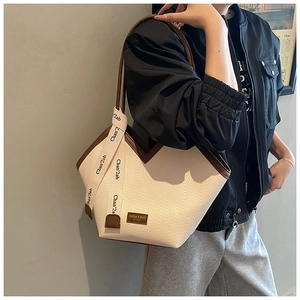 Detail of white woven tote bag featuring brown leather trim and stylish logo strap