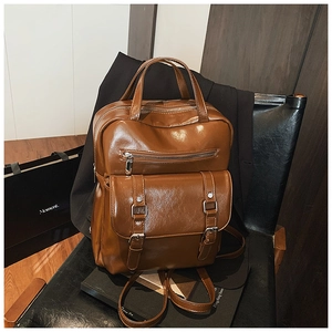 Detail of vintage brown leather backpack with silver zippers on a black chair