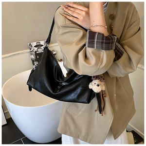 Detail of black soft leather underarm bag with cute teddy bear plush charm and silver zipper