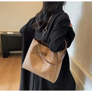 Détail du sac cabas tressé marron avec bandoulière en chaîne dorée et logo élégant