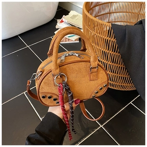 Close-up of brown suede handbag with woven rope charm and metal rivets on marble background