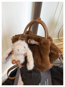 Detail einer braunen Webpelz-Handtasche mit Ledergriff und weißem Plüschhasen-Anhänger