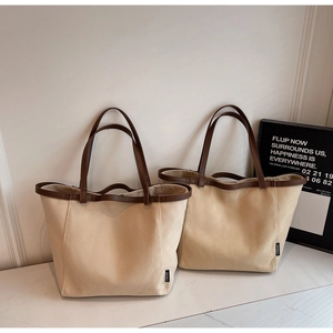 Detail view of large canvas tote bag with brown leather trim and side brand label