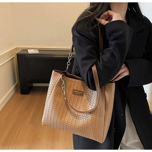 Détail d'un cabas tressé marron avec étiquette en cuir et bandoulière en chaîne métal