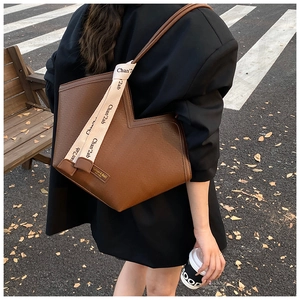 Close-up of brown leather tote bag with stylish wide woven strap on a female model