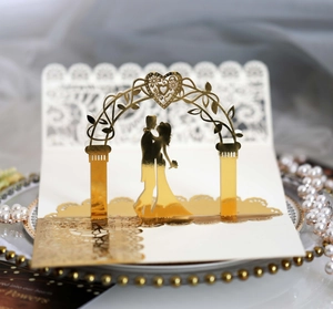 Macro shot of gold laser cut wedding card with couple silhouette under heart arch