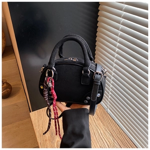 Detailed close-up of black suede Boston bag with silver rivets and woven rope charm
