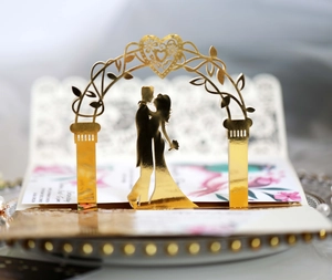 Detail of laser-cut gold mirror wedding card with silhouette of a kissing couple