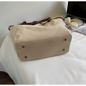 Close-up of beige canvas tote bag showing metal protective feet and leather bottom base