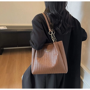 Détail du sac cabas tressé marron avec chaîne métallique et plaque de marque dorée