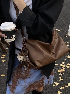 Minimalist dark brown leather shoulder bag with plush dog charm in autumn street setting