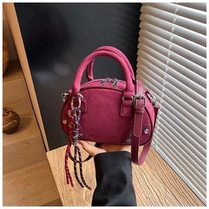 Detail of burgundy suede handbag with woven rope zipper pull on wooden surface