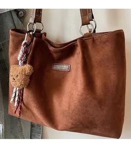 Detail of dark brown suede tote bag featuring a metallic ring and plush bear charm