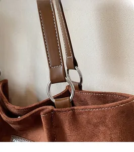 Detail of silver metal ring and white stitching on brown suede tote bag handle