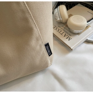 Detail of cream canvas tote bag showing tight fabric texture and side woven label