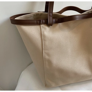 Detailed view of beige canvas tote bag with premium dark brown leather trim and stitching