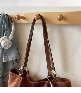 Detail of brown faux suede tote bag featuring white stitching and silver metal rings
